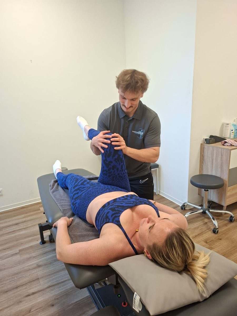 Physiotherapeutische Behandlung im Therapiepark Augsburg: Mann im Praxisshirt führt das Bein einer Frau auf der Liege